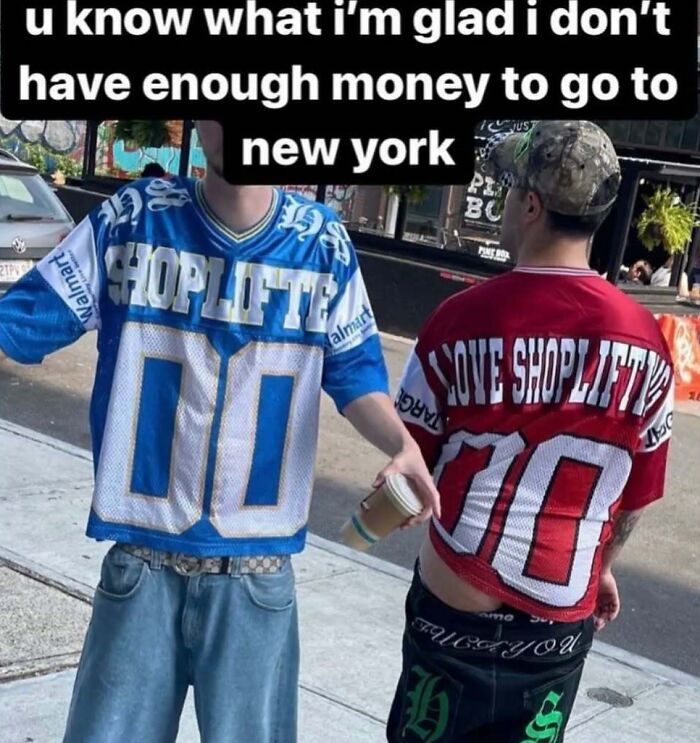 Two people wearing chaotic T-shirts with "shoplifter" messages, standing on a sidewalk.