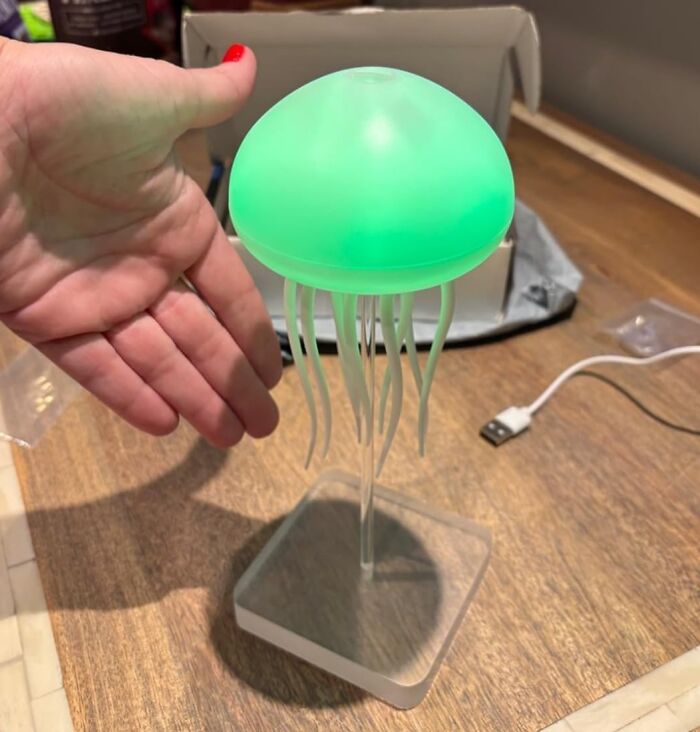 Green glowing jellyfish-shaped LED lamp on a desk, a hand next to it, showcasing a popular TikTok Shop find.