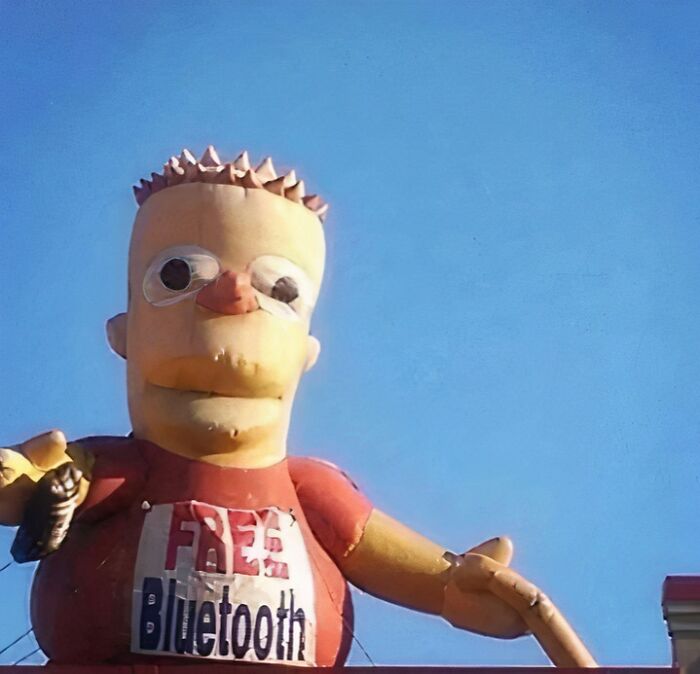 Giant cartoon character wearing a chaotic T-shirt with "Free Bluetooth" message against a clear blue sky.