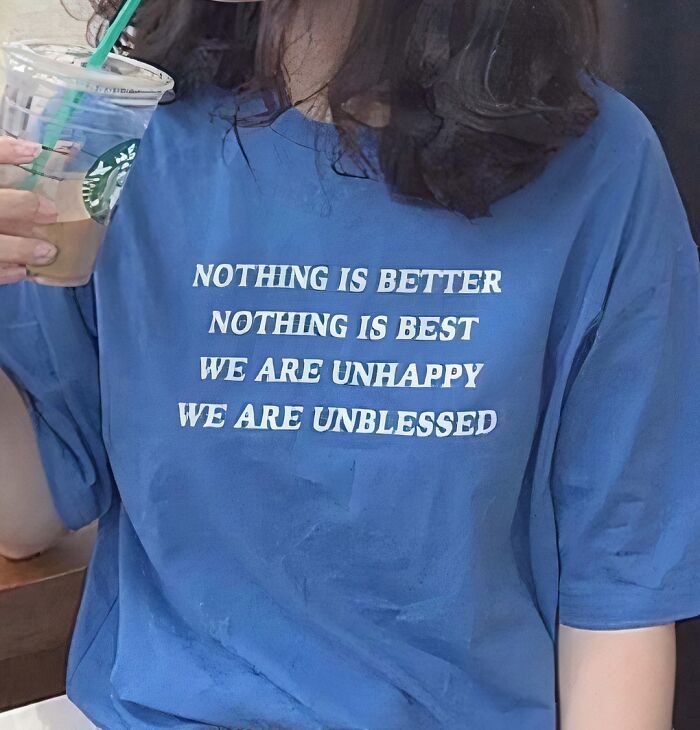 Person wearing a blue chaotic T-shirt with existential phrases, holding a Starbucks cup.