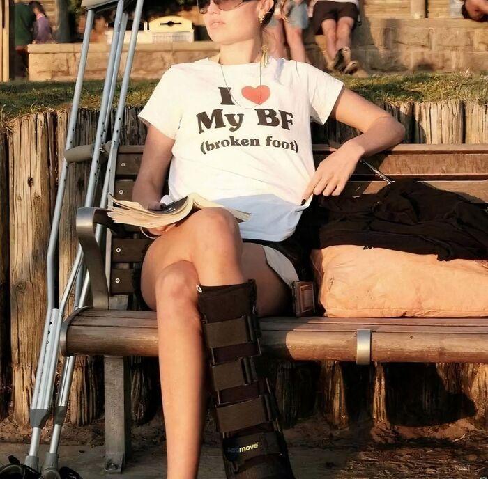 Person in sunglasses with crutches, wearing a T-shirt saying "I love my BF (broken foot)," highlighting a humorous chaotic statement.