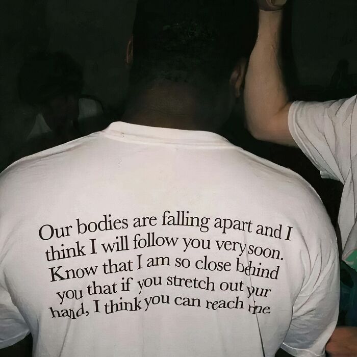 Person wearing a chaotic T-shirt with a poetic message, captured in a dimly lit setting.