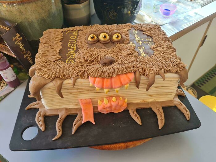 Monster book-themed cake with edible fur, three eyes, and sharp teeth, showcasing incredible bakes creativity and detail.