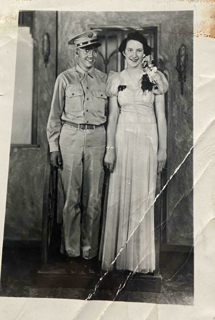 Vintage black and white photo showing a young man in military uniform with a woman in a formal gown, candid glimpses into the past.