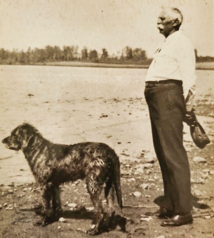 Man with vintage attire and dog standing by a lake, showcasing rare scenes from the past.