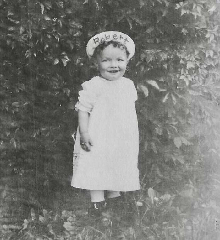 A rare photo from 50-100 years ago shows a smiling child named Robert in a dress, standing outdoors.