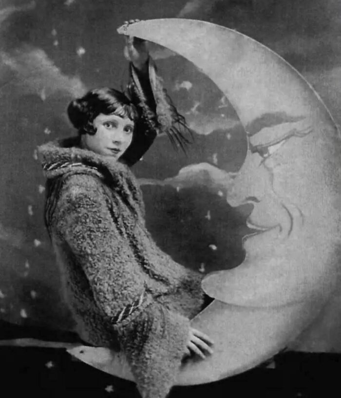 A woman in vintage attire sitting on a crescent moon prop, showcasing how the world has changed over 50-100 years.