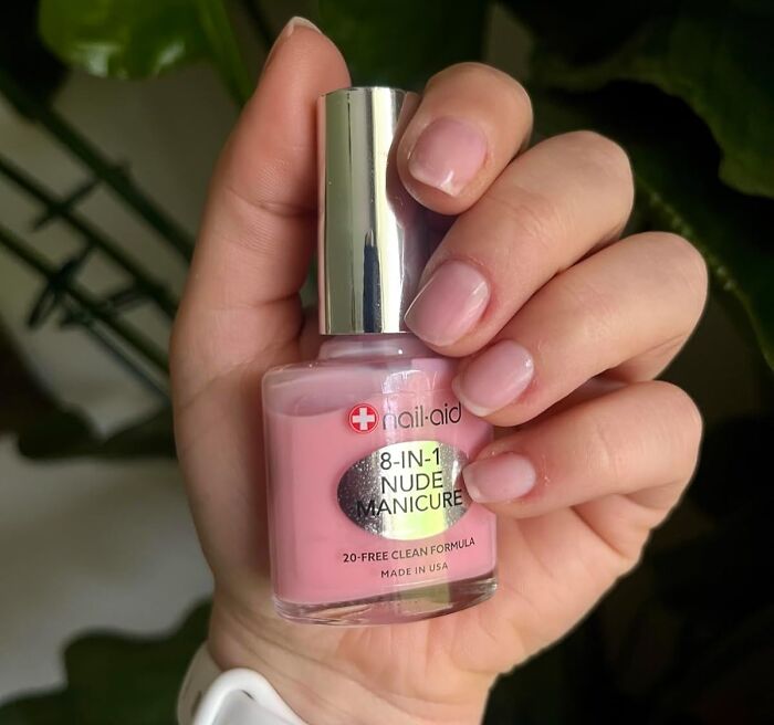 Hand holding a bottle of 8-in-1 n**e manicure polish, showcasing natural beauty product preference.