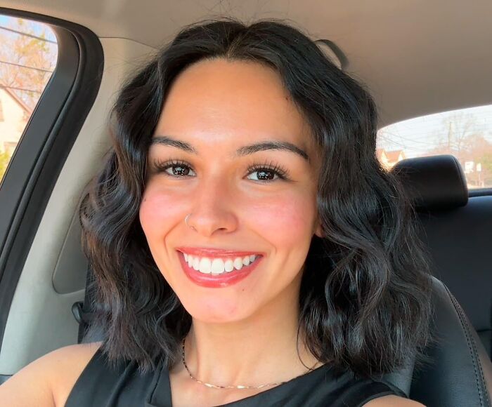 Smiling person with natural makeup, showcasing a popular beauty product look while seated in a car.