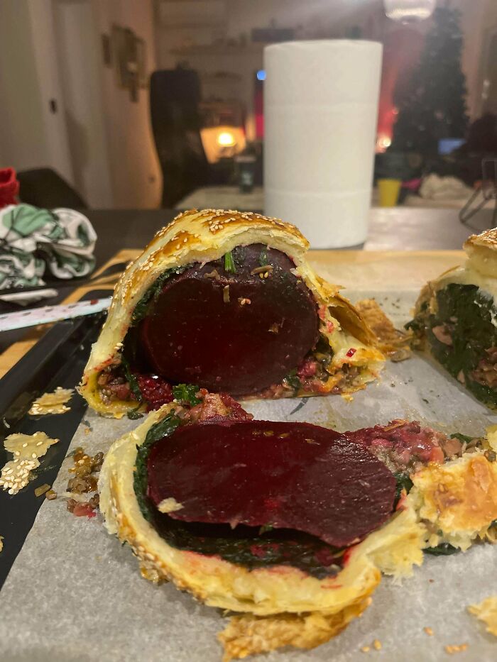 Savory pastry filled with large beet slice and greens on a baking tray, an example of unusual dishes.