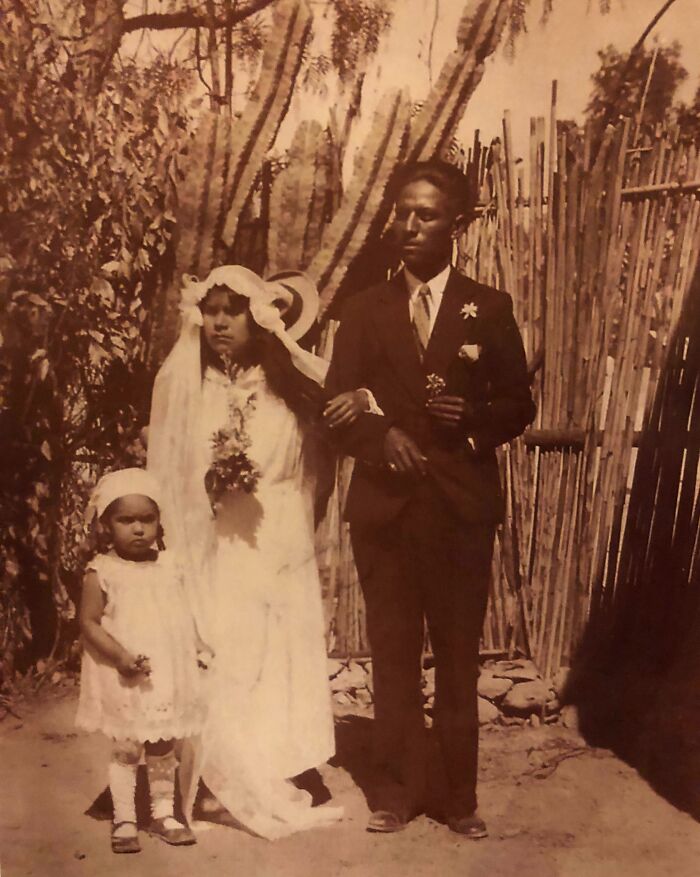 A rare photo of a wedding couple 50-100 years ago, standing with a young girl outdoors, showcasing historical attire.
