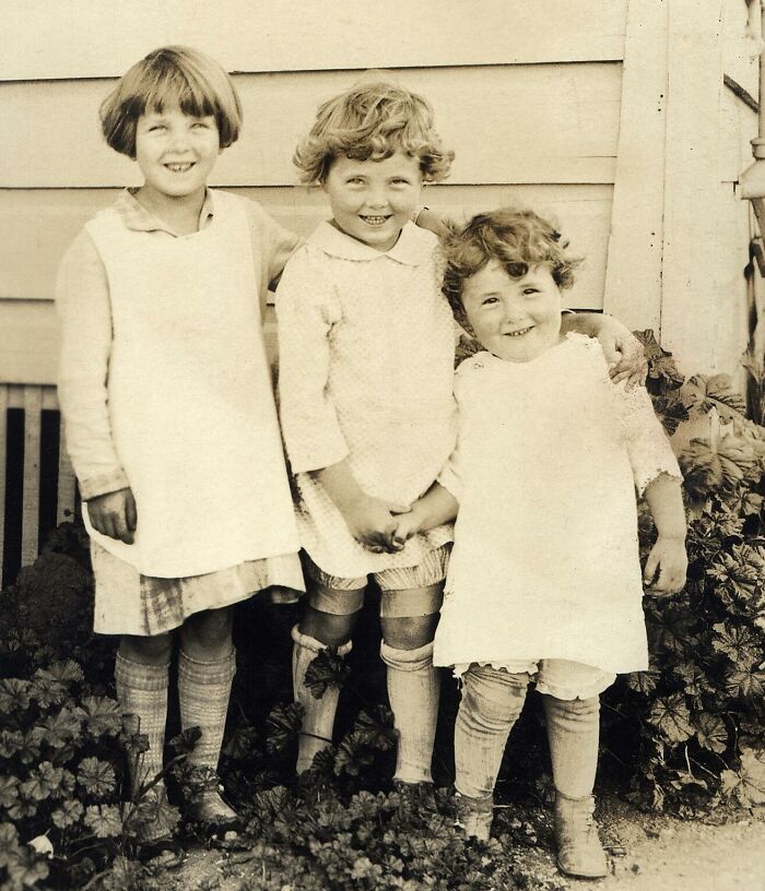 Three children smiling, dressed in vintage clothing, posing in front of an old building, illustrating rare photos from the past.