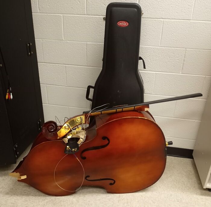 Broken double bass leaning against its case, representing a super expensive accident.