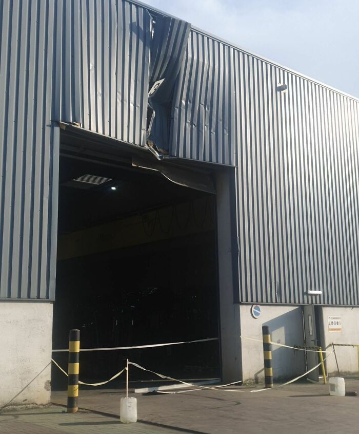 Damaged warehouse entrance after expensive accident, with dented metal siding and caution tape.