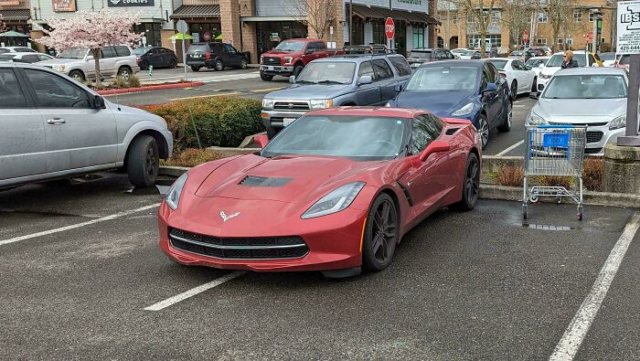 Red sports car parked across two spaces in a lot, illustrating why rich people can be shamed.