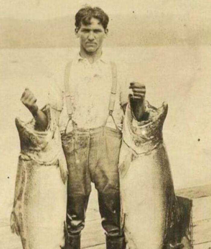 Man from early 1900s displaying two large fish, showcasing historical lifestyle change over the years.