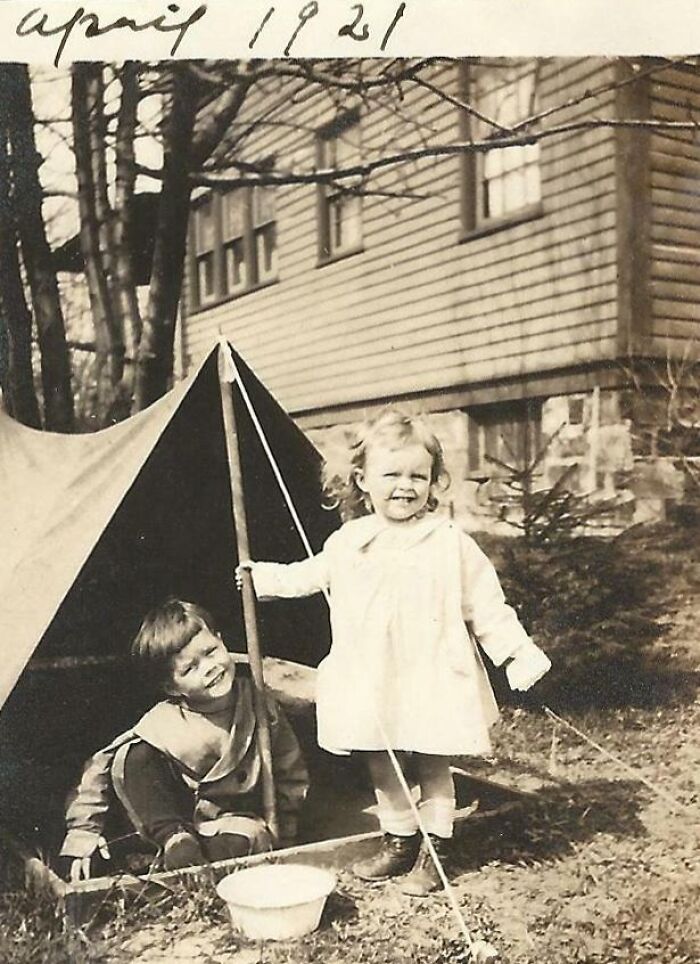 Two children playing by a tent in 1921, showcasing rare moments from decades ago.