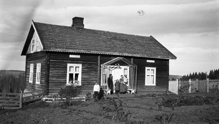 A rare old photo of a family standing outside their vintage wooden house, showcasing historical changes over time.