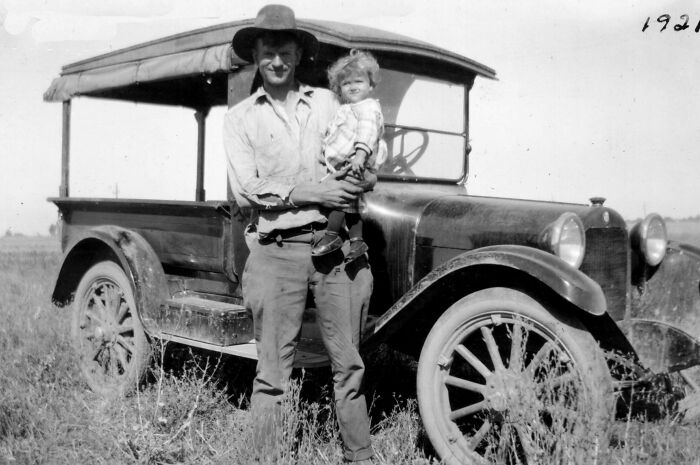 Man holding child beside vintage car, showcasing historical change over 50-100 years.