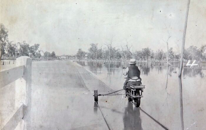 Person riding a makeshift bike on flooded road 50-100 years ago, showcasing world change over time.