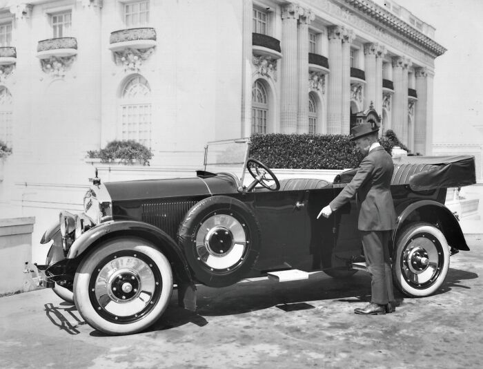 Vintage car with a man in a suit and hat, showing historical changes over 50-100 years ago.