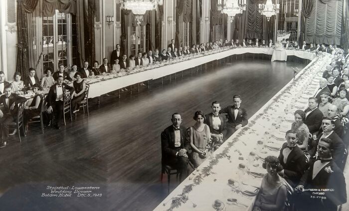 Large formal gathering from 1923 in an opulent ballroom, showcasing rare historical fashion and decor from 100 years ago.