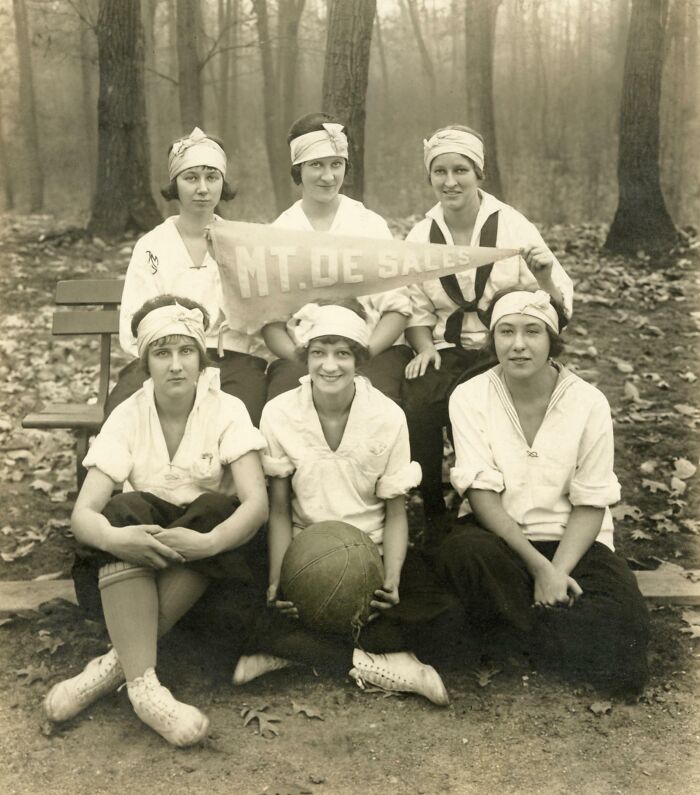 Women in vintage sports attire with a basketball and "MT. DE SALES" banner, illustrating historical changes in women's sports.