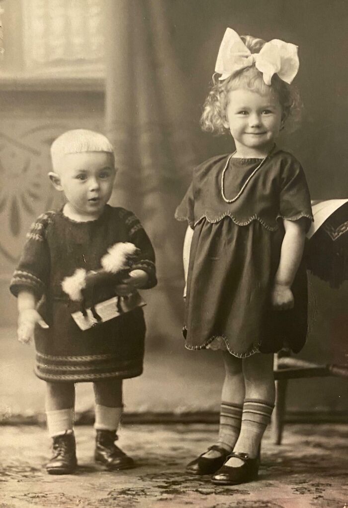 Two children from 100 years ago, a boy with a toy and a girl with a large bow, showcasing how the world has changed.