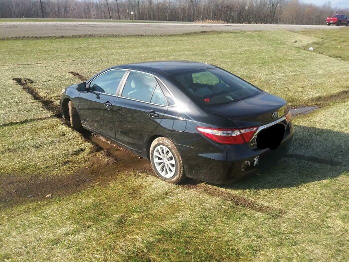 Black car stuck in muddy grass near a road, illustrating someone's worse day.