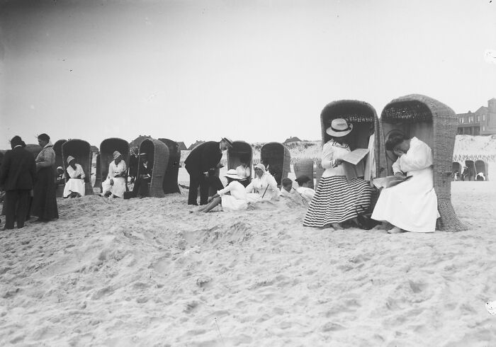 People in vintage beach attire sitting in wicker beach chairs, illustrating how much the world has changed over decades.