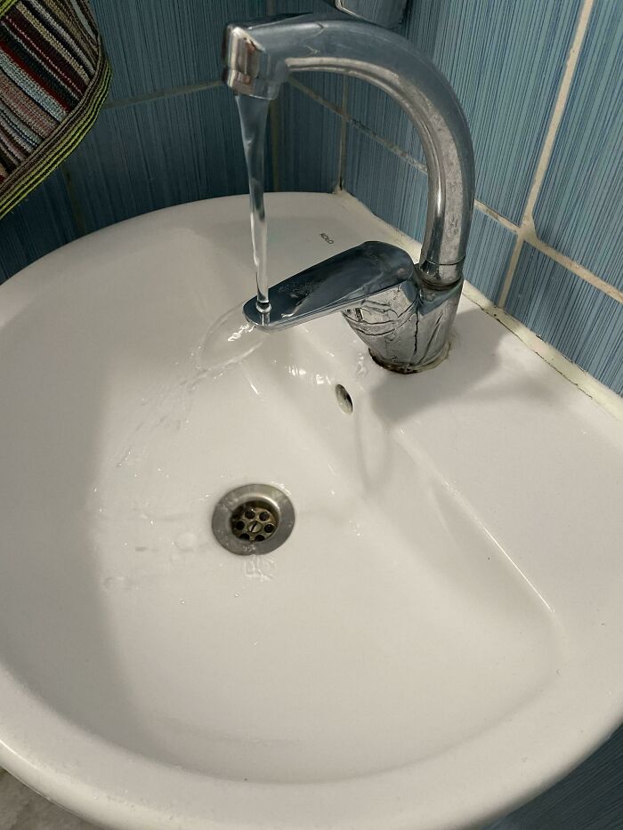 Bathroom design fail with faucet misaligned over sink, water missing the drain.