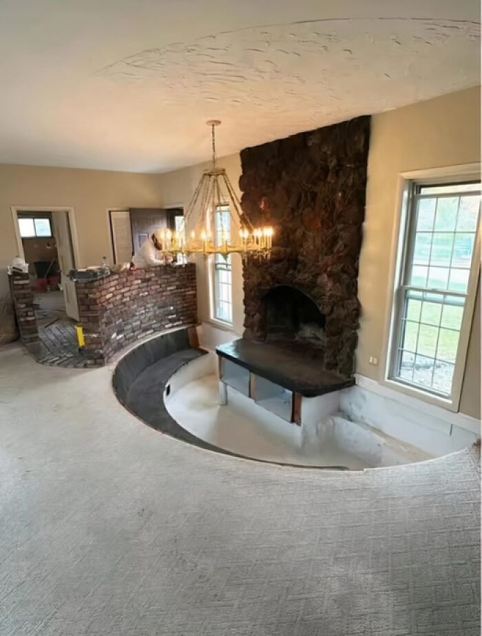 Sala con diseño extraño, escalón elevado frente a chimenea y candelabro, ejemplo de arquitectos fracasados.