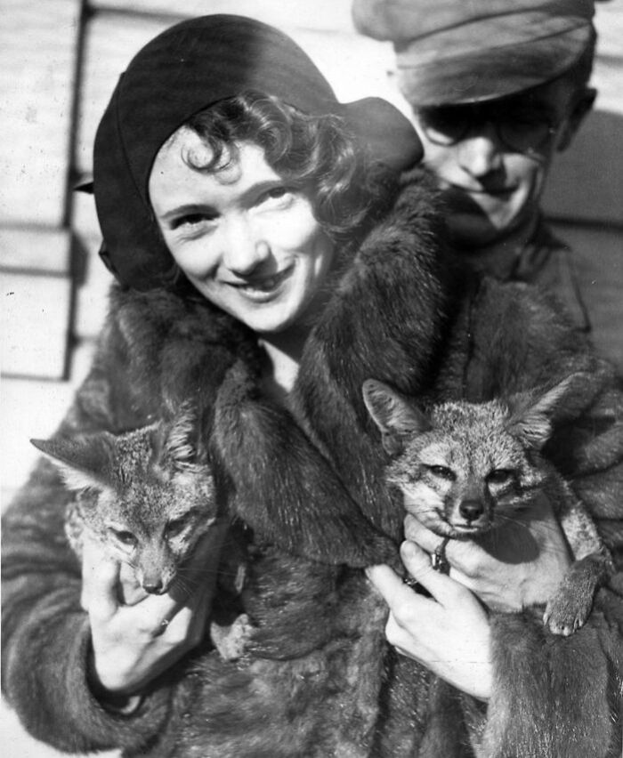 Woman holding foxes, smiling as a man stands behind. Rare historical photo showing change over 50-100 years.