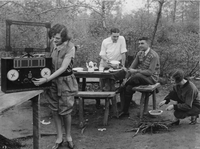 Vintage photo of people camping, adjusting an old radio, showing historical lifestyle changes over 50-100 years.