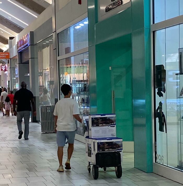 Person in a mall pushing a cart with boxes, possibly representing shameless scams.