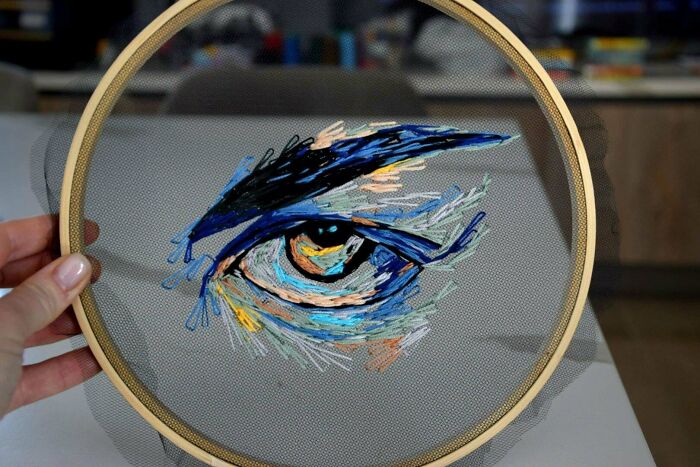 Hand holding embroidery hoop showcasing an eye design with colorful and intricate embroidery skills on fabric.