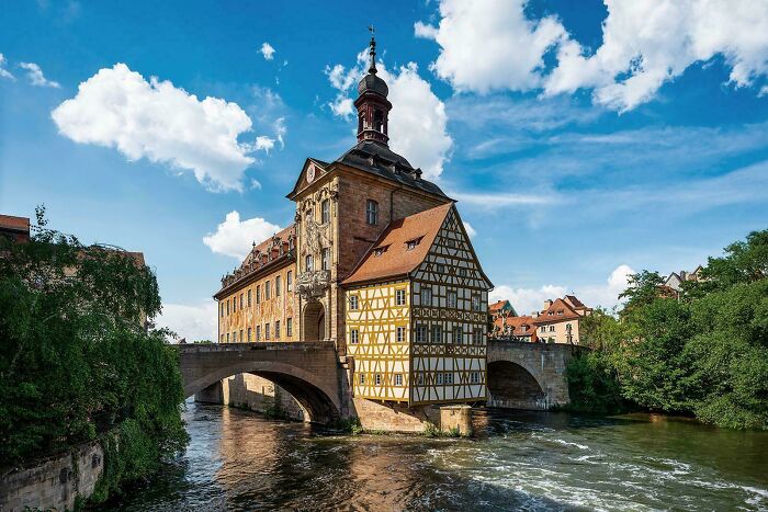 Historic architectural feat of a timber-framed building situated on a stone bridge over flowing water under a blue sky.