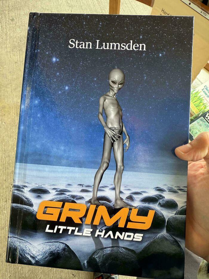 Alien-themed terrible book cover titled "Grimy Little Hands" held by a person.