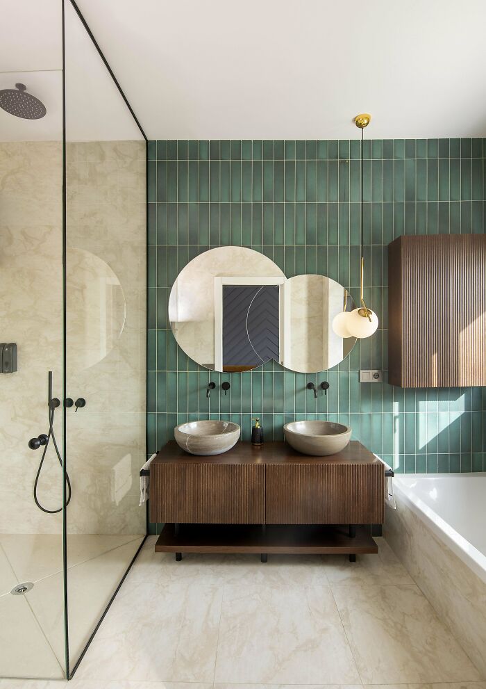 Modern bathroom with green tiled wall, round mirrors, vessel sinks, and wooden vanity in a beautifully decorated home.