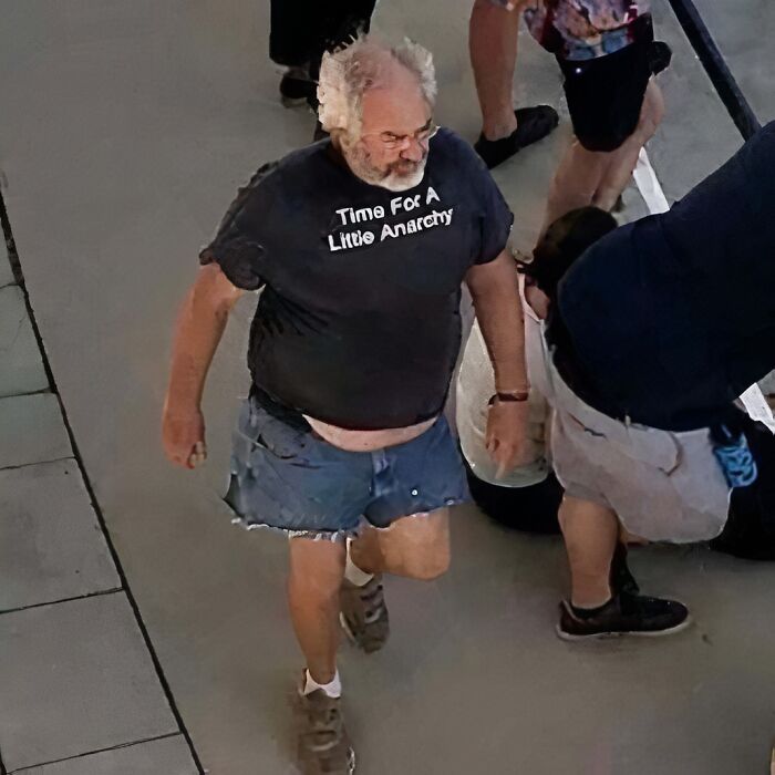 Man in a chaotic T-shirt reading "Time For A Little Anarchy," walking in denim shorts.