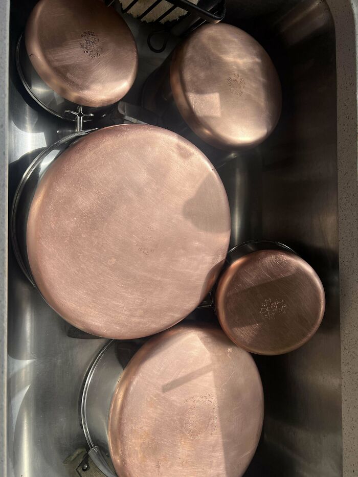 A collection of various sizes of "Buy It For Life" copper pots and pans in a metal sink, shiny and clean.