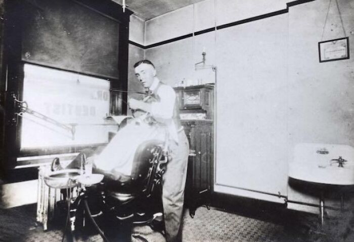 Vintage photo of a dentist's office with a dentist attending a patient, showcasing historical change.