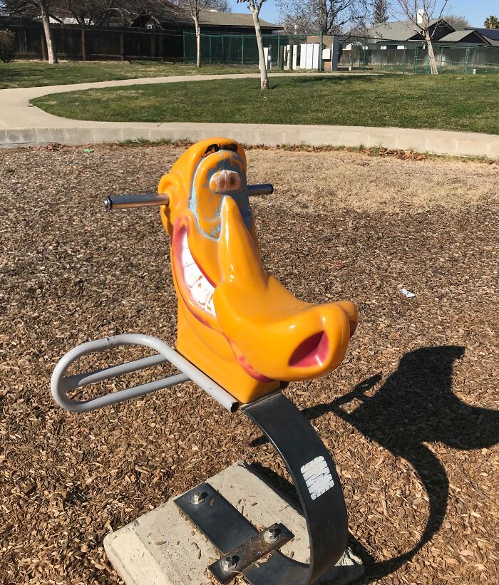 Playground design fail with a distorted cartoon character ride in a park setting.