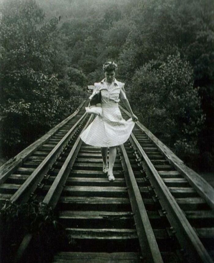 A person in vintage attire walking on a railway track surrounded by trees, highlighting rare photos from 50-100 years ago.