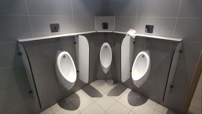 Design fail with three urinals awkwardly positioned in a small bathroom corner.