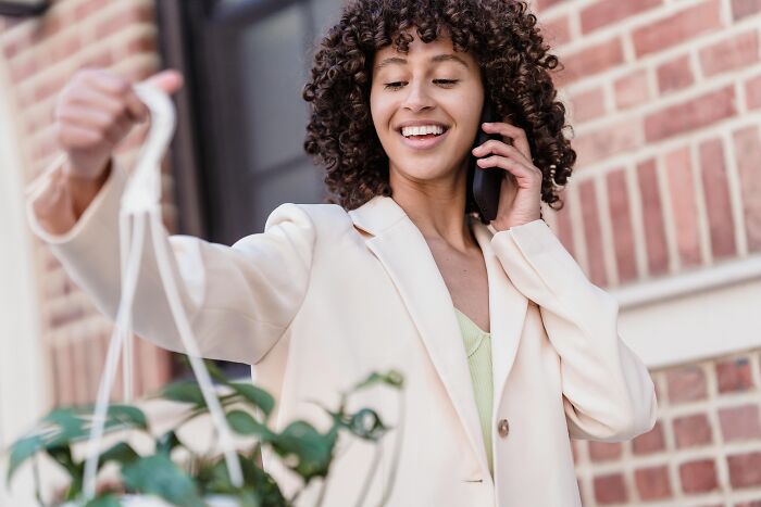 Smiling woman on phone holds plant, embodying simple approaches to enhance life.