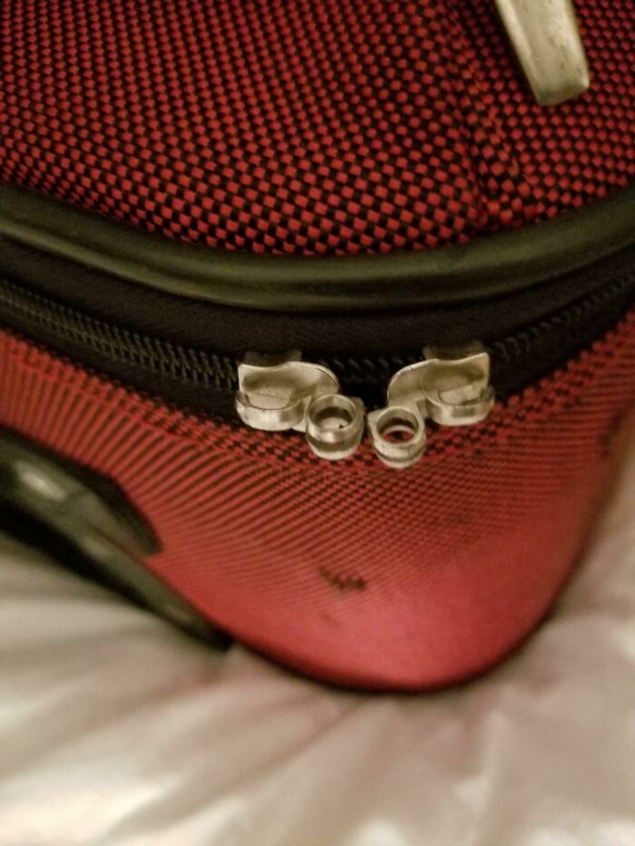 Broken airline baggage zipper on red suitcase.