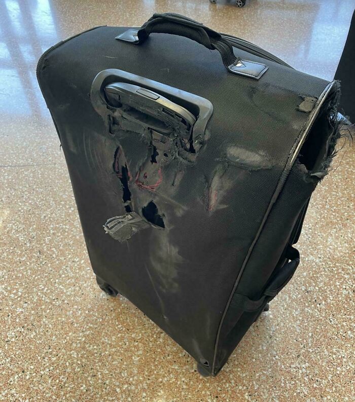 Damaged airline baggage with large tears and scratches on a suitcase at the airport.