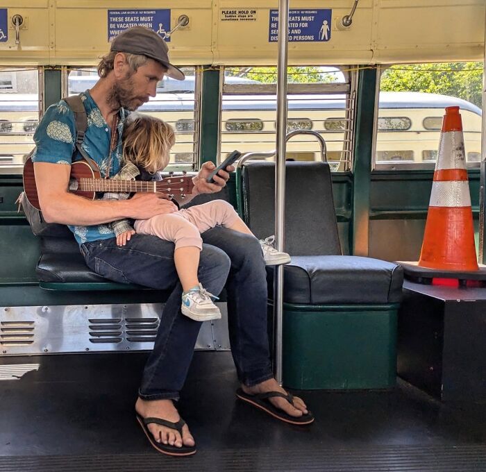 Father and child on a San Francisco streetcar, father strumming a ukulele, capturing urban life through Sage Akaboshi’s lens.