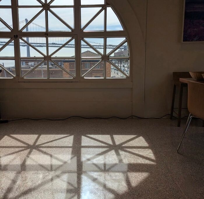 San Francisco view through arched window, bridge visible, captured by photographer's lens, sunlight casting shadow patterns.